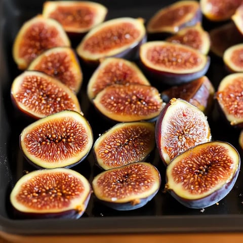 A close-up image of halved figs arranged on a black tray, showcasing their vibrant interior.