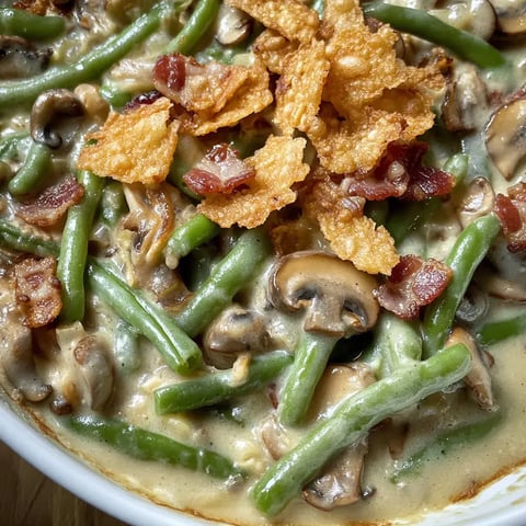 A close-up of a creamy green bean casserole topped with crispy bacon bits and fried onion pieces.