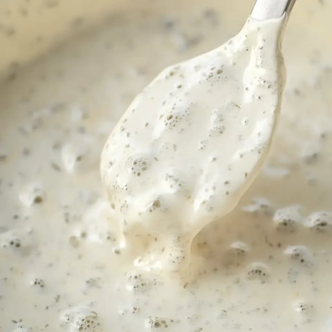A close-up of a spoon lifting creamy, frothy batter or sauce from a bowl.